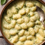 Plate of creamy pesto gnocchi garnished with fresh basil and Parmesan cheese